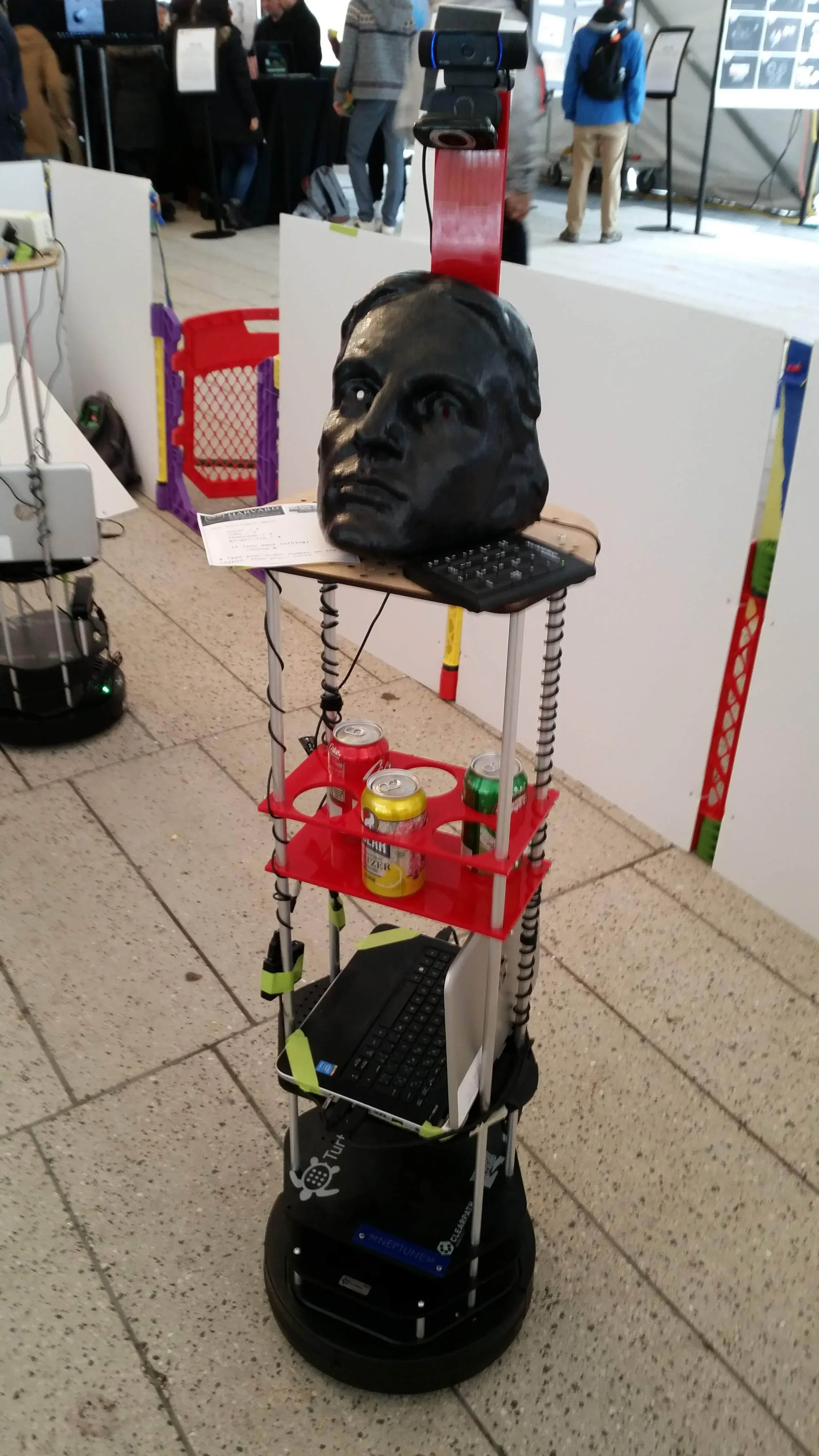 TurtleBot waiter at a design fair with a serving tray, cameras, and a John Harvard mask.